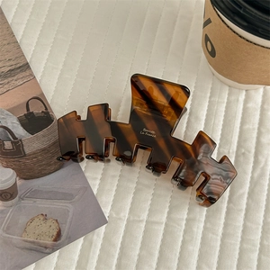 Detail of a large amber tortoiseshell hair claw clip with golden text on white background