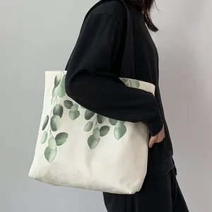 Detailed view of large white canvas tote bag with green eucalyptus leaf print on shoulder