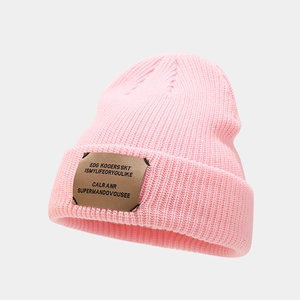 Close-up of pink ribbed knit beanie featuring a brown leather patch with logo detail