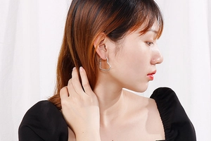 Close-up of a silver heart-shaped earring worn by a model on a white fabric background