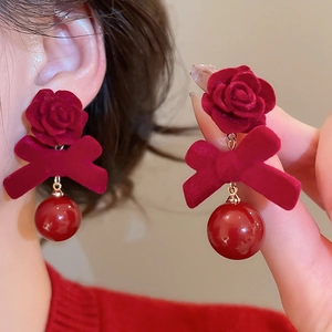 Détail de boucles d'oreilles nœud en velours rouge avec pétales de rose et perles chic