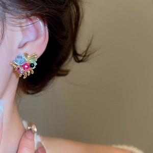 Close-up of colorful flower stud earrings with blue, red and green petals on gold stem