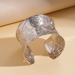 Detail of wide silver metal cuff bracelet featuring intricate floral paisley embossing