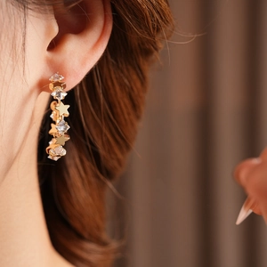 Detailed view of gold C-shaped earrings with sparkling stars worn by a female model