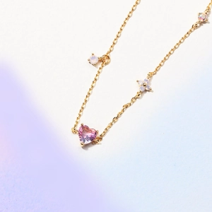 Macro shot of gold bracelet featuring heart pink zircon and white opal flower charms