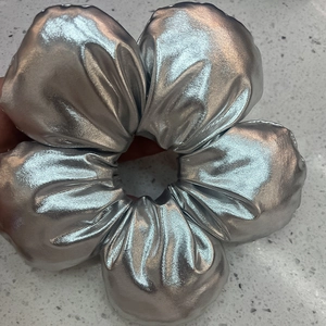 Close-up of a silver metallic fabric scrunchie showing detailed pleated texture and shine