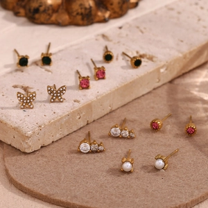 Detail of gold floral stud earrings with pink and green crystals on a stone surface