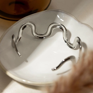 Detail of silver wavy irregular open bangle bracelet placed on a white ceramic dish