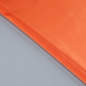 Detail of the orange dress showing smooth silk-like fabric texture and precise stitching