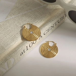Close-up of golden concentric circle earrings with crystal on book near sunglasses