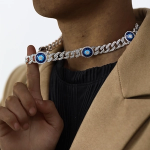 Iced out silver Cuban link necklace featuring a blue evil eye pendant on male model