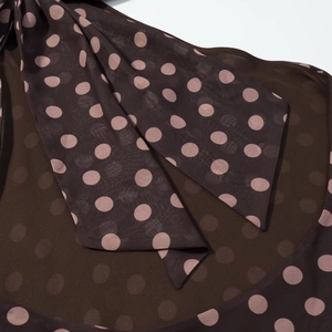 Details des kaffeebraunen Polka-Dot-Chiffonstoffs mit rosa Schleife am Ausschnitt