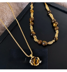 Dettaglio del ciondolo in occhio di tigre su catena dorata a treccia e collana di perle