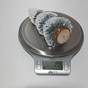 Close-up of mini flocked cedar Christmas tree with wooden base on scale weighing 17.9g