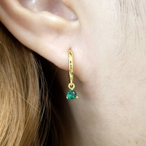 Macro shot of gold hoop earrings with round green zircon drop on ear with blonde hair