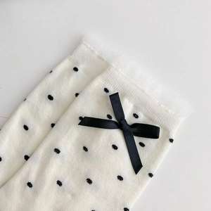 Gros plan de chaussettes blanches à pois avec nœuds en satin noir et bordure en dentelle