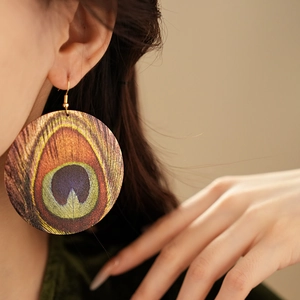 Close-up of wooden bohemian peacock feather pattern earrings worn by a female model