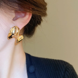 Detail view of golden C-shaped metallic wavy earrings worn by a model in soft lighting
