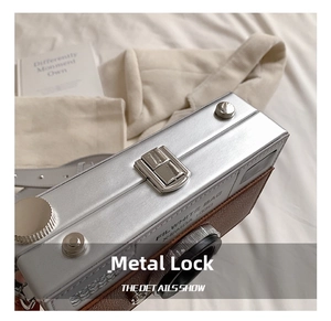 Detail of metal buckle on camera-shaped crossbody bag with silver and brown stitching