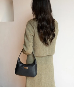 Detail of black lychee grain leather shoulder bag with gold hardware on olive coat