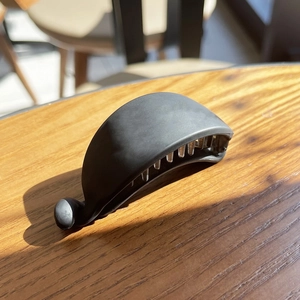 Matte black banana clip hair accessory on a wooden table with soft indoor shadows