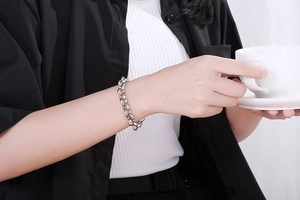 Detail of silver oval link titanium steel bracelet worn by model holding a coffee cup