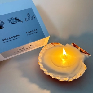 Detailed view of a lit shell-shaped candle with its branded English Pear orchid gift box