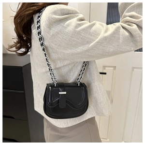 Side view of a black leather crossbody bag with silver chain strap worn by a model
