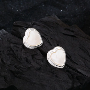 Elegant heart-shaped silver stud earrings with white mother of pearl on a dark stone