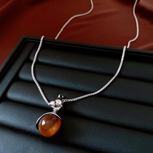 Detail von Bernsteinfarbenem Anhänger mit Silberkette auf luxuriöser roter Seide und Leder