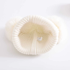 White knitted baby beanie with dual plush pom poms and internal acrylic material label