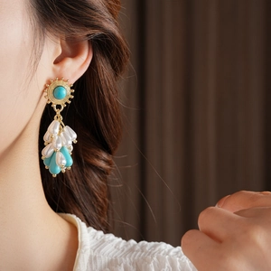 Detail of vintage bohemian drop earrings with turquoise beads and pearl tassels on a model