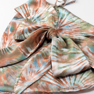 Detail of satin fabric showing orange and blue tie-dye print and decorative knot