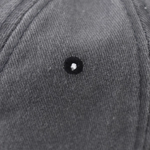 Dettaglio macro dell'occhiello ricamato sul berretto in cotone grigio lavato vintage