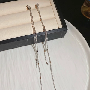 Detailed view of silver long chain tassel earrings on a textured jewelry display plate