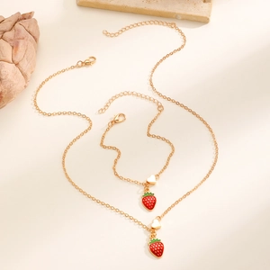Dettaglio di set collana e bracciale dorati con ciondoli a fragola in smalto rosso e cuore