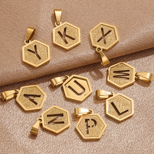Golden hexagonal initial pendants with matte sandblasted finish on brown silk fabric