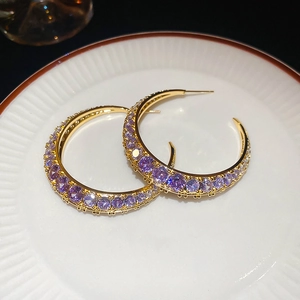 Detailed close-up of large gold C-shape earrings with purple zircon on white ceramic