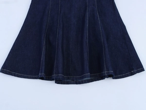 Détail de l'ourlet de la robe en jean bleu foncé montrant les coutures et la texture