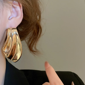 Detail of large gold liquid metal fishtail earrings with irregular wrinkled texture