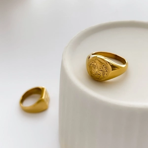 Detailed close-up of gold signet rings with vintage embossed portrait on white ceramic base