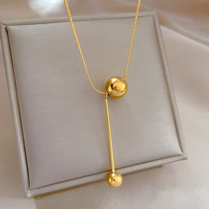 Detailed close-up of a gold titanium steel necklace with tassel ball pendant on a soft cushion