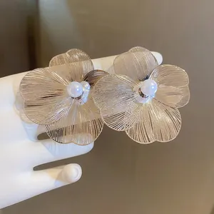 Elegant gold flower earrings with layered petals and a pearl center shown in hand