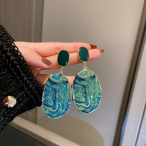 Macro shot of blue-green textured geometric earrings with gold trim and silver pins