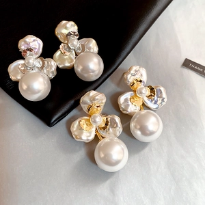Detail view of gold-plated flower stud earrings with large white pearls on black leather