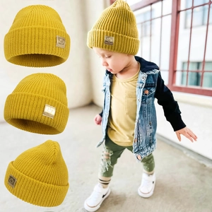 Knitted yellow children beanie featuring a smiley face patch and rolled cuff design