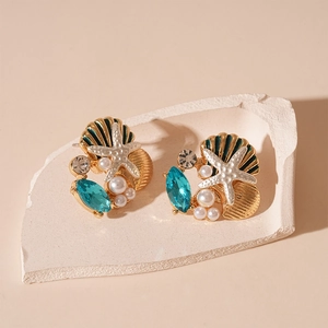 Détail de boucles d'oreilles océan avec étoile de mer, coquillage et perle bleue
