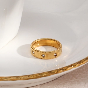 Détail d'une bague large plaquée or 18 carats avec étoiles en zircon sur assiette blanche
