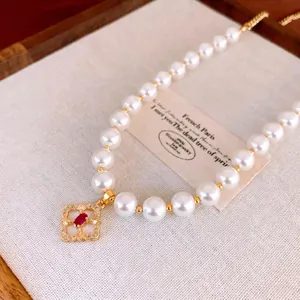 Elegant gold-plated pearl necklace with a red gemstone clover pendant in a luxury setting