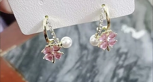 Macro view of pink four-leaf flower earrings with white pearl and gold pave accents